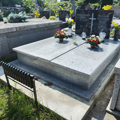 Pomnik z granitu srebrzystego i ciemnymi napisówkami, oddzielonymi krzyżem